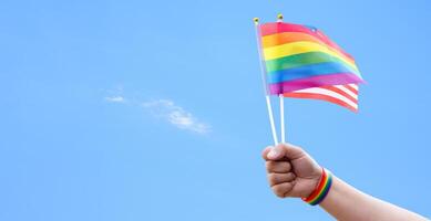 Rainbow flags and American flag showing in hands against clear bluesky, copy space, concept for calling people to support and respcet the genger diversity and celebrate lgbtq in pride month. photo
