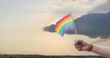 Rainbow flags showing in hands against clear bluesky, copy space, concept for calling all people to support and respcet the genger diversity, human rights and to celebrate lgbtq in pride month. photo