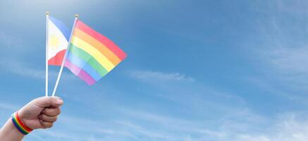 Rainbow flags and Philipines flag showing in hands against clear bluesky, copy space, concept for calling people to support and respcet the genger diversity and celebrate lgbtq in pride month. photo