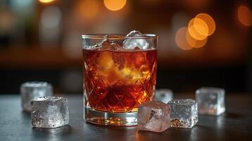 A glass of amber-colored liquid sits on a table, accompanied by several ice cubes, set against a blurred, warm-toned background. photo