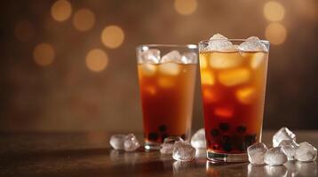 Two glasses of iced tea with tapioca pearls, on a table with scattered ice cubes, set against a softly blurred background. photo