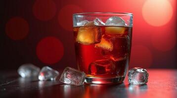 A glass filled with a dark, refreshing beverage, garnished with ice cubes, set against a vibrant, blurred red background. photo