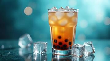 Transparent glass filled with amber liquid and ice, placed on a reflective surface with a blurred background. photo
