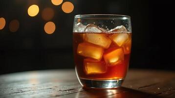 Glass with brown liquid and ice cubes on table. photo