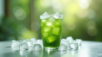 A vibrant green beverage in a glass adorned with ice cubes on a reflective surface set against a blurred, sunlit backdrop. photo