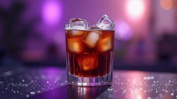A glass filled with ice cubes and a dark liquid sits on a glittery surface, with a blurred bokeh background. photo