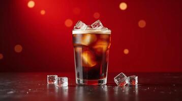 A glass filled with a dark beverage, garnished with ice cubes, presented against a vibrant red background. photo
