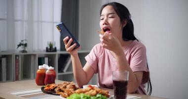 Relaxed young woman enjoy crispy fried food while casually scrolling through mobile phone in living room at home. video