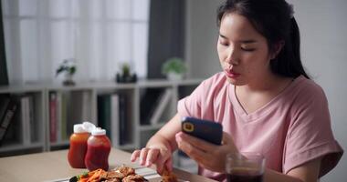 Handheld shot, Asian woman enjoys fried food while playing with mobile phone during a casual meal. video