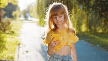 Smiling child girl using smartphone typing text answering messages chatting online in street video
