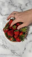 A hand reaches for fresh strawberries in a bowl on a marble surface, evoking freshness, summer, and healthy eating Caucasian adult vibrant video