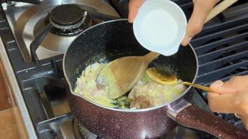 A person stirs a creamy sauce on a stovetop, adding ingredients with a wooden spoon culinary techniques and home cooking are featured video