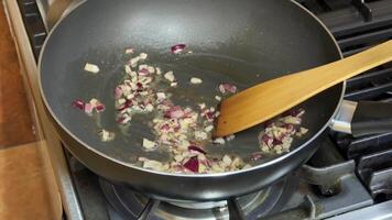 Chopped onions sauteing in a frying pan on a stove, capturing a culinary preparation moment with a wooden spatula video