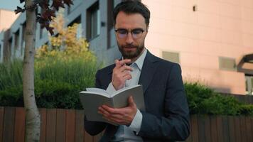 Thoughtful pensive man Caucasian businessman business coach in city write notes in notebook university professor writer thinking writing ideas at paper notepad smiling prepare for class lesson outside video