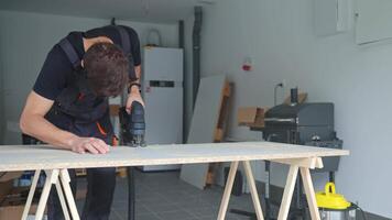 Worker using handheld cordless electric jigsaw to cut wooden board in garage. Skilled carpenter working in workshop. Man doing DIY home renovation video