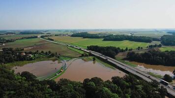 Aerial view of highway with car traffic running alongside flooded zone in rural farmland landscape. Concept of climate impact, infrastructure vulnerability and transportation challenges video