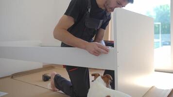 Focused man connecting parts of bed during home furniture assembly, surrounded by minimal tools and packaging. Handyman assemblies white bed frame on floor video