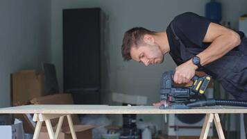 Man in workwear using jigsaw to cut chipboard panel in modern home workshop. Concept of DIY renovation, craftsmanship and home improvement process. video