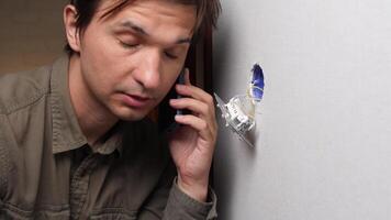 A man talking on a cell phone while looking at a hole in the wall video
