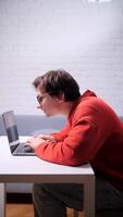 A man in glasses is sitting at a table with a laptop, A man with poor eyesight stares at a screen video