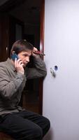 vertical eletricista falando em Móvel telefone enquanto instalando ou reparação luz interruptor dentro apartamento, segurando alicate dentro de outros mão e olhando às elétrico caixa video