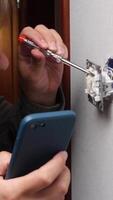 vertical A man looks at instructions on his phone online on how to fix a switch, electrical wiring himself. A man fixes electrical wiring at home. A man fixes a switch himself. video