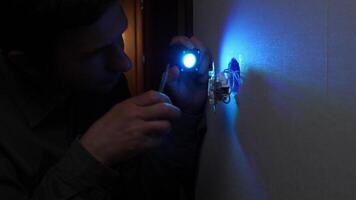 Electrician working in the dark, using a small flashlight and screwdriver to repair a light switch set into a white wall, ensuring proper electrical connections for safe operation video