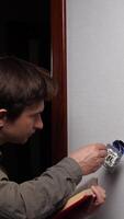 vertical Electrician installing a light switch on a white wall, carefully consulting the instruction manual while performing essential home repair and renovation tasks, ensuring safety and precision video