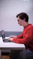 A man in glasses is sitting at a table with a laptop, man putting on glasses before working on computer video