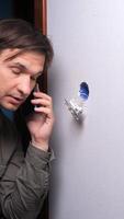 vertical Electrician is making a phone call while inspecting an electrical outlet with exposed wiring, potentially seeking guidance or reporting a problem video