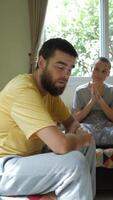 Sad man sitting on couch while partner scolds him in background video