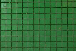 Close-up of a green ceramic tiled wall with visible grout lines and minor surface imperfections, ideal for backgrounds or design elements. photo