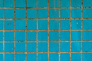 Square blue ceramic tiles with worn grout and surface scratches, creating a gritty, urban wall texture for design and architectural backgrounds. photo