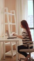 un joven mujer tipos a su organizado hogar oficina escritorio, creando un inspirador atmósfera. natural ligero aumenta su concentración y creatividad, maximizando productividad mientras teletrabajo video