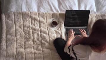 A relaxed person is typing on a laptop in bed, with a steaming cup of coffee beside them, blending comfort and focus in their cozy workspace to maximize productivity on important tasks video