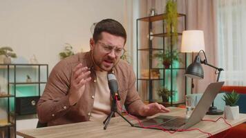 Young positive Caucasian man blogger singer using laptop while singing into microphone at table video