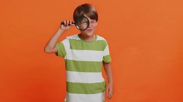 Child boy kid holds magnifying glass near face looking at camera with big zoomed eye, analyzing video