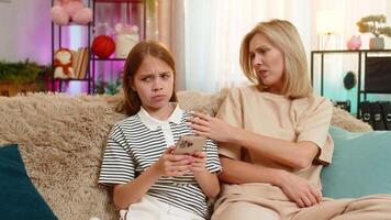 Child girl kid playing mobile game with mother on home sofa reacting emotionally to character losing video