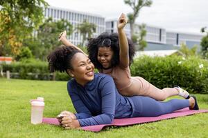 African American mother and young daughter are lying down and playing ride after having yoga exercise public park for weekend leisure and happiness photo