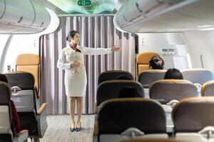 Asian flight attendant demonstrating safety procedure showing emergency exit before taking off in the airplane for cabin crew and airline business photo