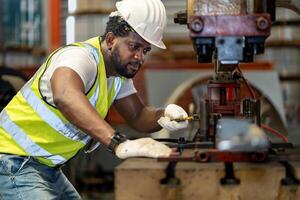 African American industrial worker is fixing hydraulic power press machine to make metal and steel part while working inside the metal sheet galvanized roof factory for safety industry photo