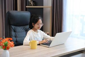 Young asian schoolgirl doing her class homework assignment at home using laptop computer for education and study concept photo