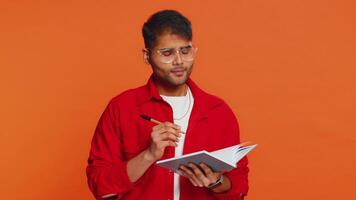 Thoughtful Indian man making notes, writing down thoughts with pen into notepad notebook, good idea video