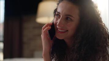 Caucasian woman smiling curly girl calling mobile phone in bed morning conversation hotel bedroom relaxed female talk friendly cellphone chatter gossip at home apartment laugh communicate answer call video