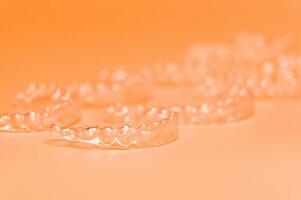 Orthodontic silicone aligner background. Advertisement of invisible braces retainer. Medical website concept. Pros and cons of aligners. peach saturated background photo