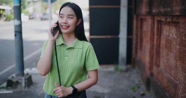 Handheld shot, Cheerful young woman happily talks on the phone while walking on a sidewalk in the city. video