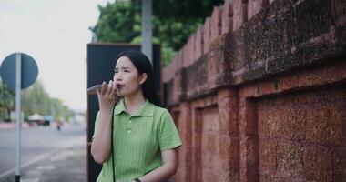 Handheld shot, Young Asian woman happily talks on the phone while walking on a sidewalk in the city. video