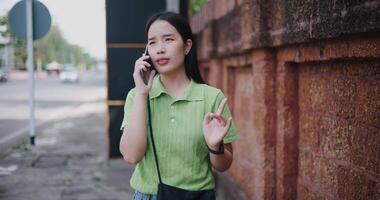 Cheerful young woman happily talks on the phone while walking on a sidewalk in the city. video
