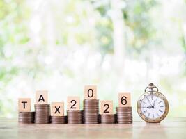 Vintage watch, Wooden blocks with the word TAX, Nunber 2025 and stack of coins. The concept about saving money and manage time to paying tax in year 2026 photo