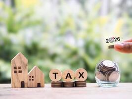 Wooden blocks with the word TAX and stack of coins. The concept of payment tax for house, Property investment, House mortgage, Real estate in year 2026 photo